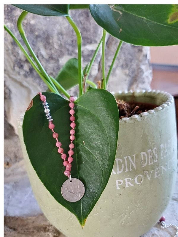pink gemstone coin necklace on a green plant
