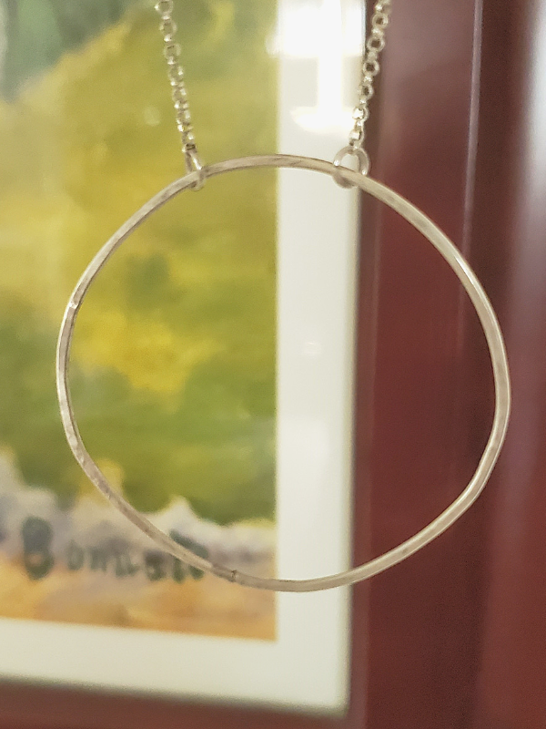 silver circle necklace in front of framed wall art