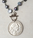 up close Blue-gray pearl necklace with a silver French coin on white wood