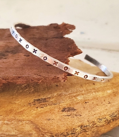 Silver XOX cuff bracelet on wood and stone
