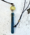 teal green gemstone stick black cord necklace on white distressed table