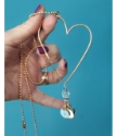 hand holding gold heart charm necklace on teal background