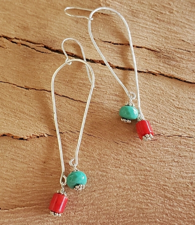 silver elongated loop earrings with red and teal gemstones on wood