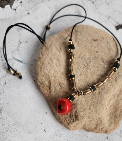 Red sponge coral, brass beads, black cord necklace on rock