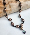 brown pearl necklace knotted on black leather with a mystic topaz pendant on wood