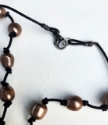 brown pearl necklace knotted on black leather clasp on white background