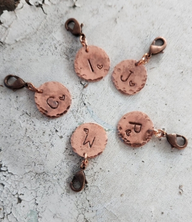 Handcrafted copper initial charms on rustic white background