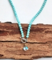 aqua blue beads surround rainbow quartz pendant necklace on wood