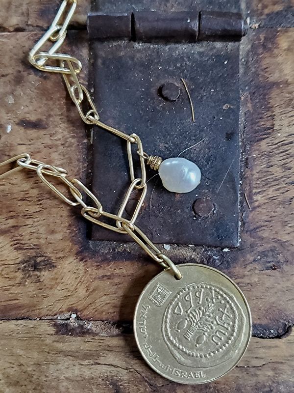 gold coin necklace with white pearl on old trunk