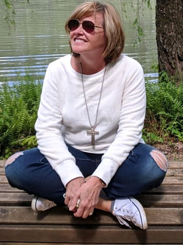 sitting on a dock in blue jeans and a unique cross necklace