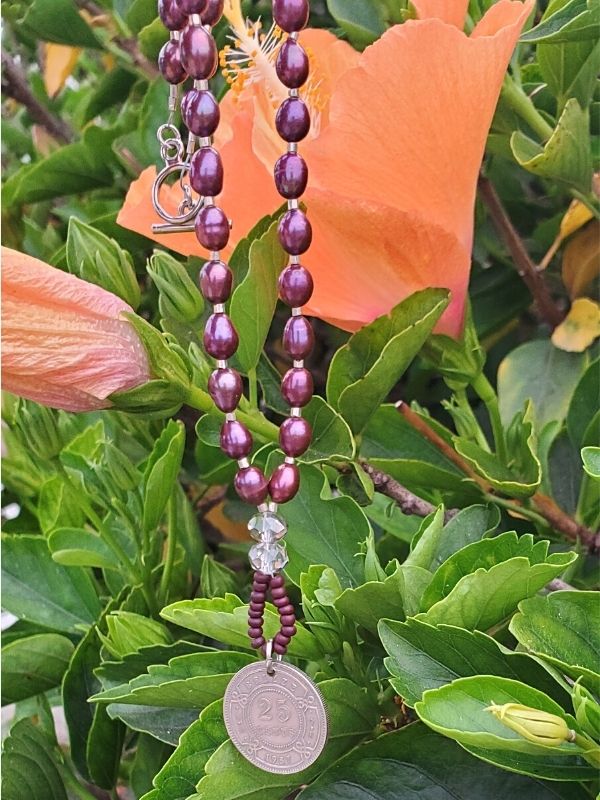 Purple pearl Belize coin necklace hanging on flowering plants