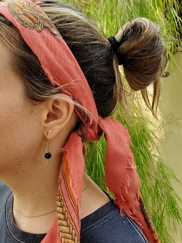 wearing a long scarf with hair in a bun and black earrings