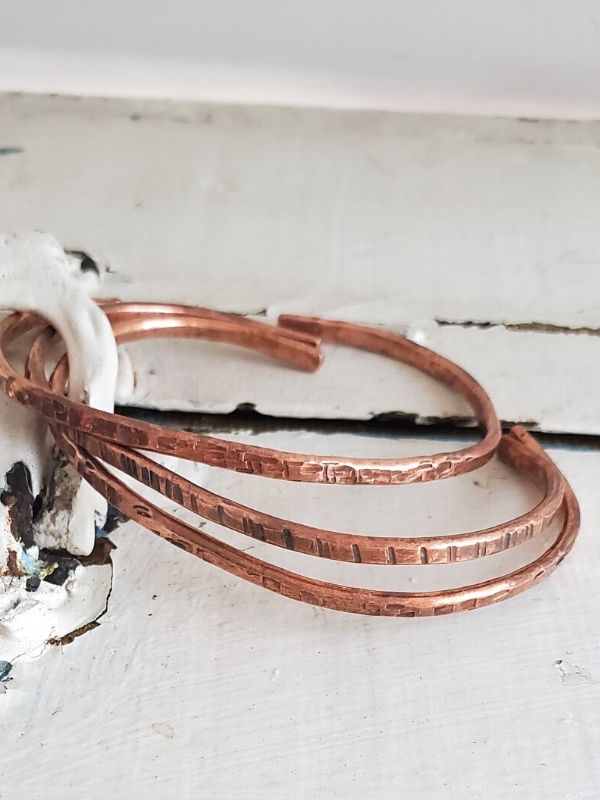 three hammered copper cuffs on white wood