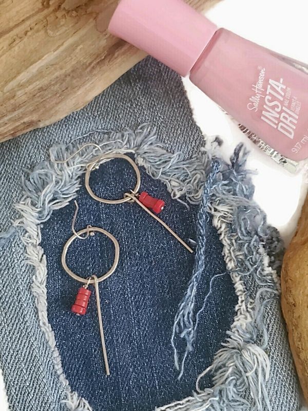 silver hoop stick earrings with pink nail polish on denim