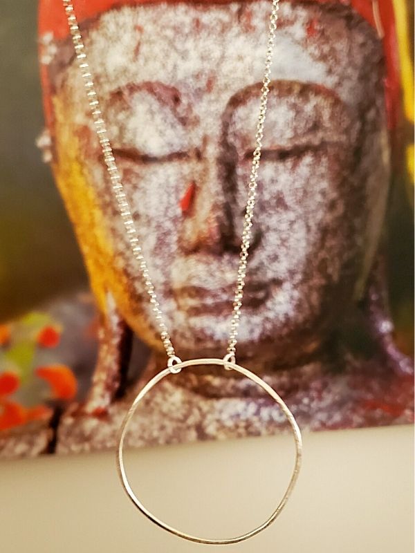 silver circle necklace hanging by Budha painting