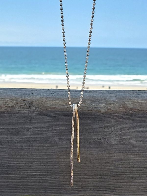 silver gold stick necklace on post at beach