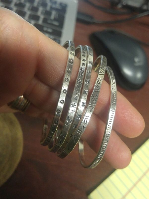 holding silver textured cuff bracelets by lap top