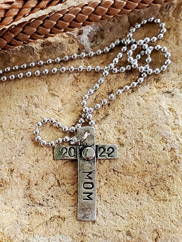 unisex stamped silver cross necklace on rock