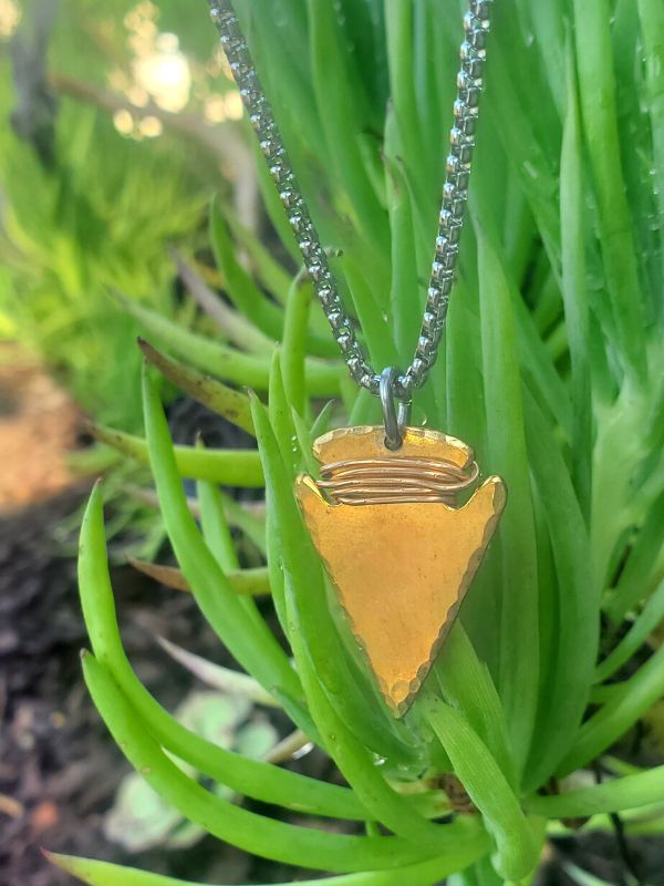 bronze arrowhead necklace hanging on a plant